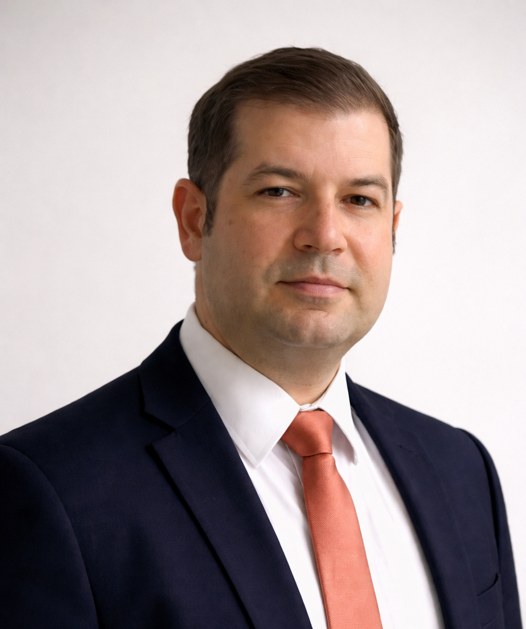 Professional studio headshot of a consultant in a navy suit, white shirt and salmon tie