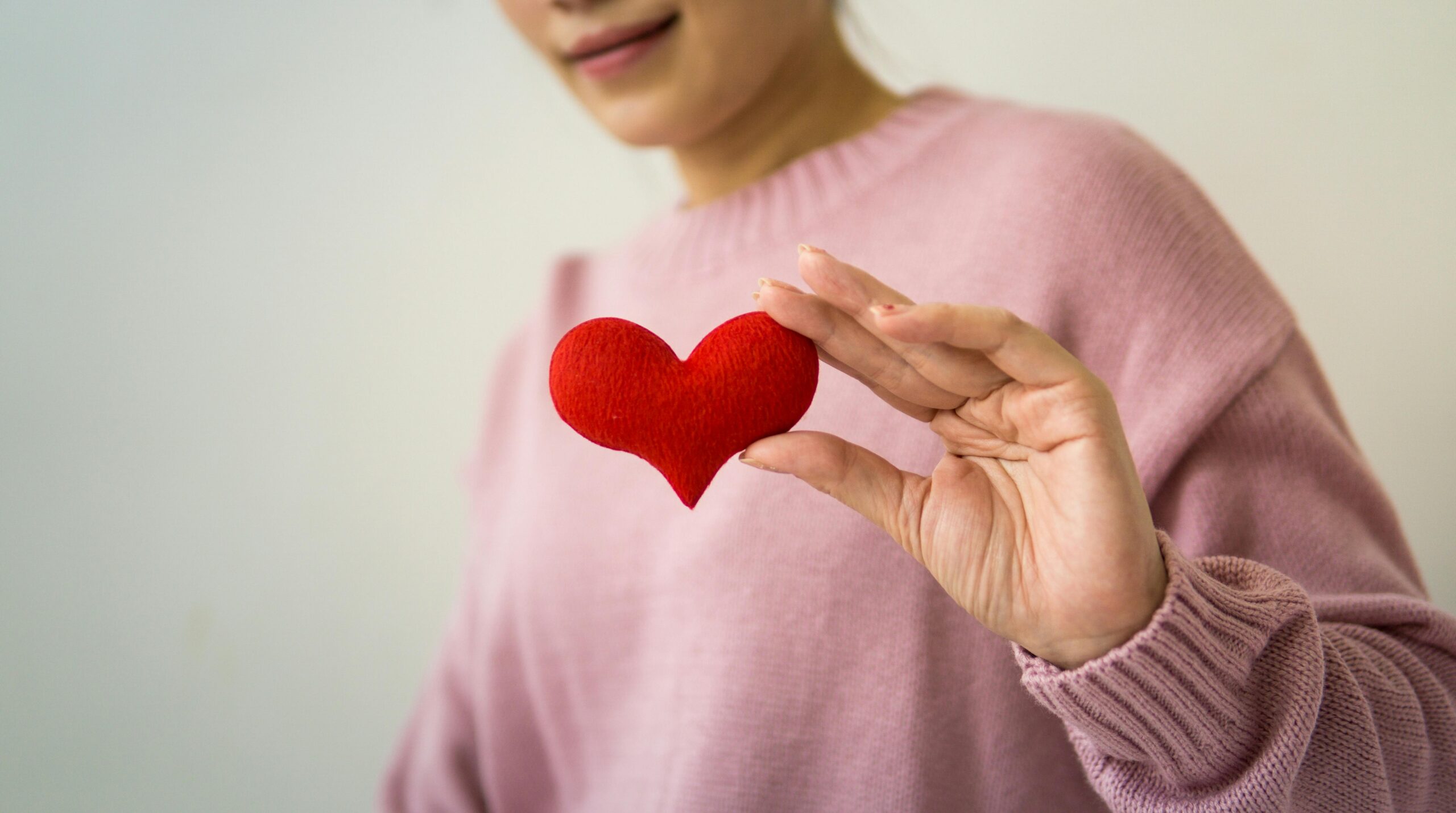 Close-up of a smiling woman holding a small red heart symbol, representing expert cardiology care and cardiovascular well-being at the London LSDC Healthcare clinic.