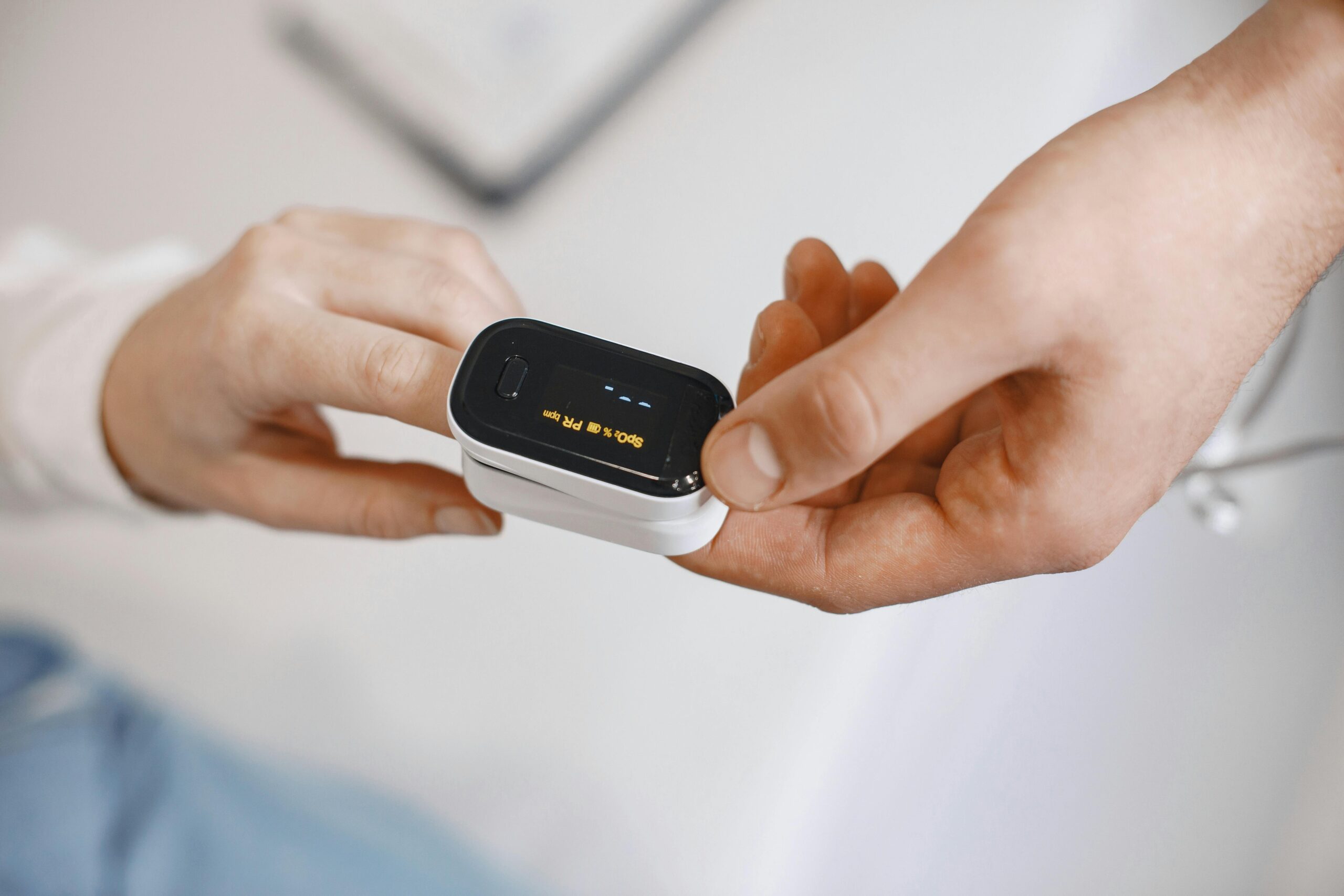 Close-up of a healthcare professional placing a digital pulse oximeter on a patient's finger to measure blood oxygen saturation and heart rate.
